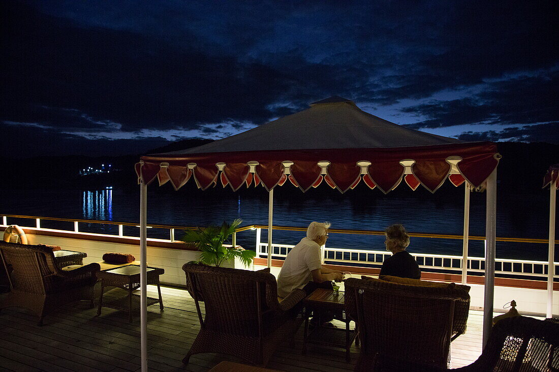 Guests relax under canopy on deck of Ayeyarwady (Irrawaddy) river cruise ship Anawrahta (Heritage Line) at night, near Ngayiphyo, Sagaing, Myanmar