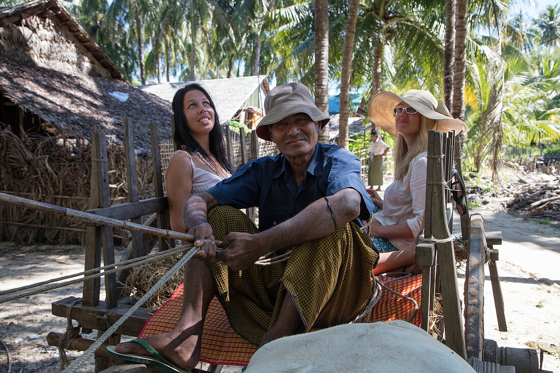Touristen fahren auf Ochsenkarren durch Dorf Maung Shwe Lay, nahe Ngapali, Thandwe, Myanmar