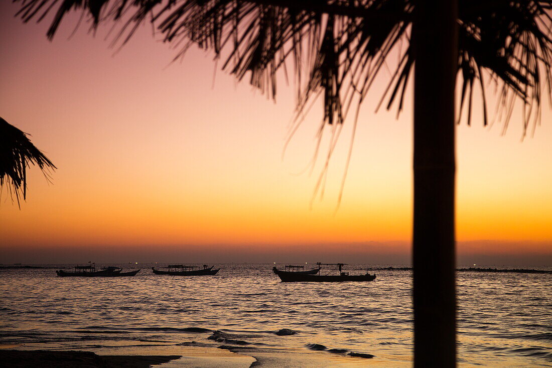 Silhouette von strohgedeckten Sonnenschirm der Yoma Cherry Lodge und Fischerboote am Strand Ngapali Beach bei Sonnenuntergang, Ngapali, Thandwe, Myanmar
