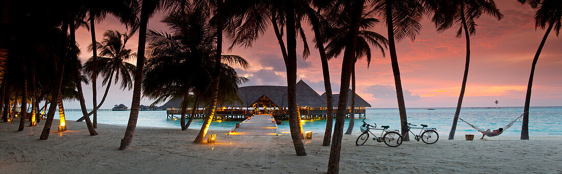 Stelzenrestaurant im Meer hinter Palmen in Gili Lankanfushi Insel bei Sonnenuntergang