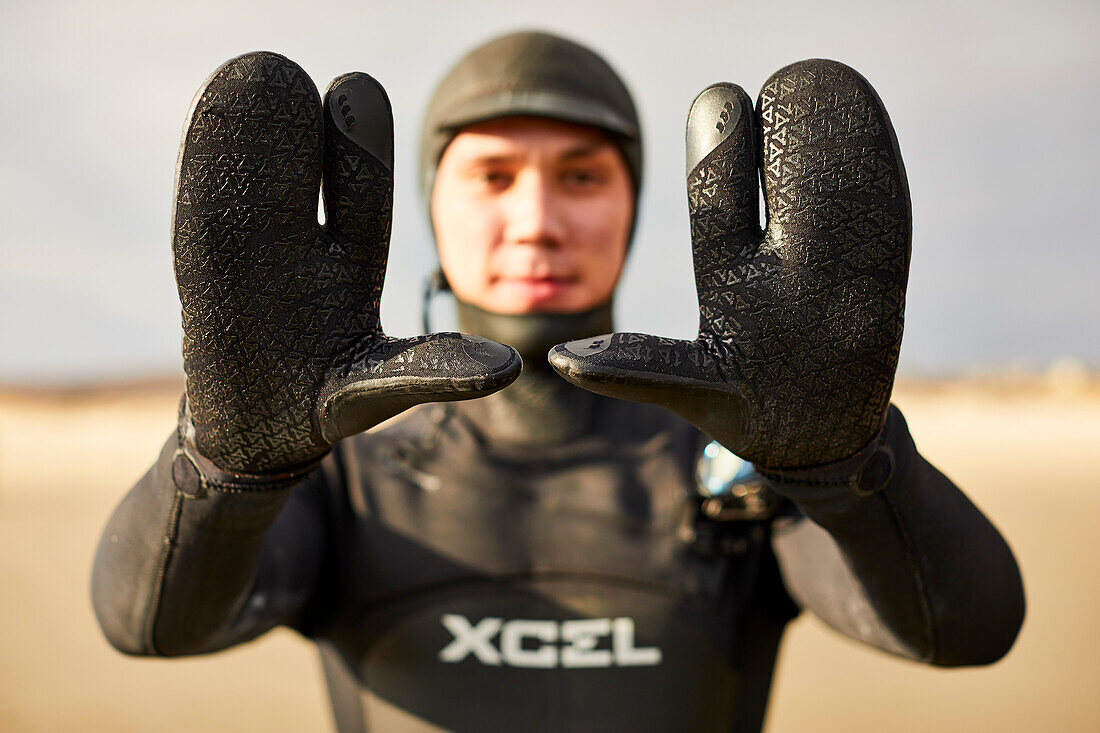 Ein männlicher Surfer zeigen seine kalten Wetter-Handschuhe