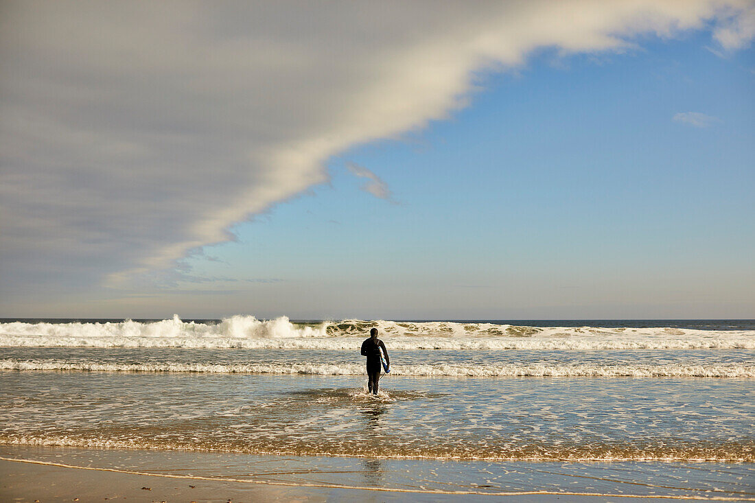 Ein Surfer, der in Richtung Meer am guten Hafen-Strand in Gloucester, Ma geht