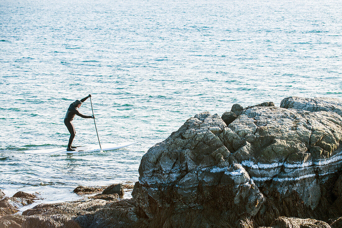 A paddleboarder paddleboarding off the coast of Maine on a cold winter day