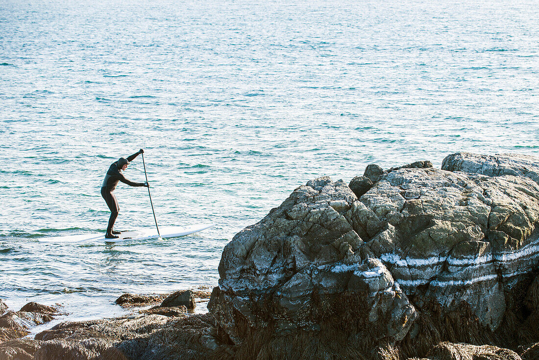 Ein Paddleboarder Paddleboarding vor der Küste von Maine an einem kalten Wintertag