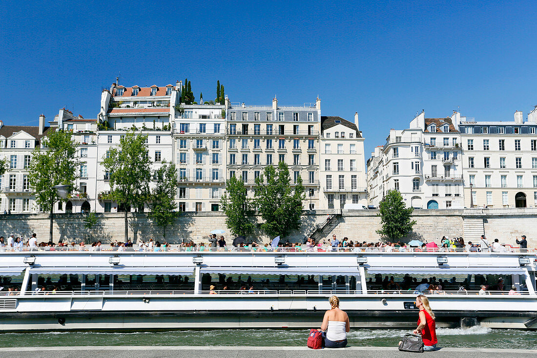 France, Paris. 5th arrondissement. Tourists looking at a passing boat. In the background the Ile Saint Louis.