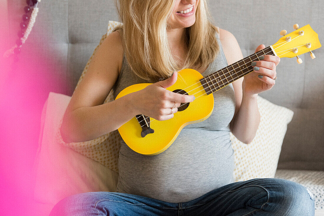 Caucasian and expectant mother playing small yellow guitar