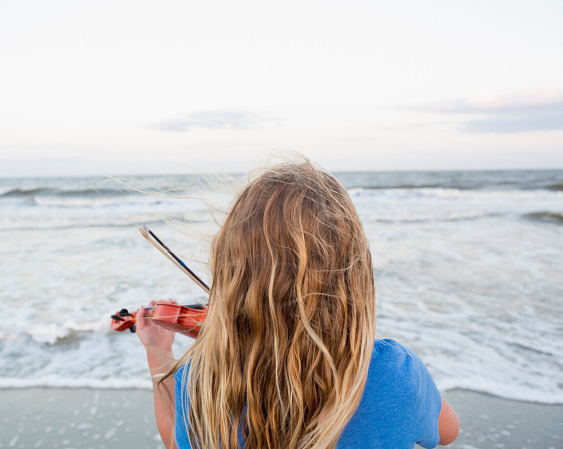 Rear view of Caucasian girl playing violin at beach