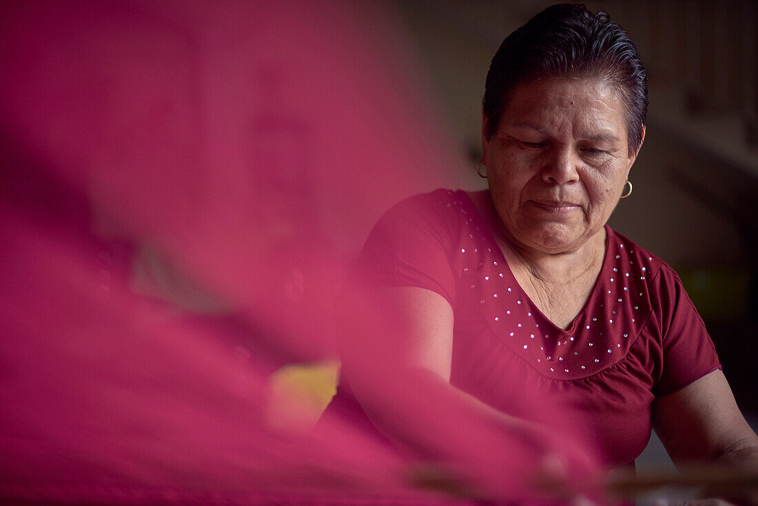 Hispanic woman weaving fabric on loom