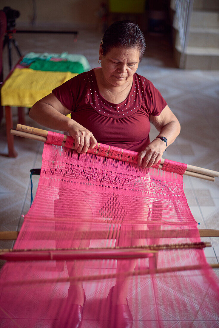 Hispanic woman weaving fabric on loom