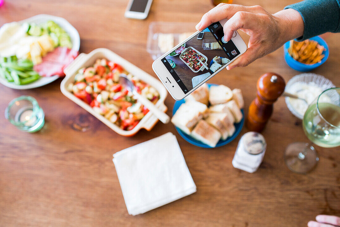 Woman photographing appetizers on table with cell phone