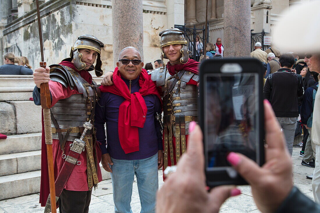 Asiatischer Tourist posiert mit Männern in römischen Gladiatorkostümen und läßt sich mit Smartphone fotografieren, Split, Split-Dalmatien, Kroatien, Europa