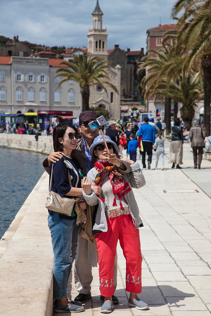Asian couple take selfie photograph with smartphone and selfie stick on seafront promenade, Split, Split-Dalmatia, Croatia