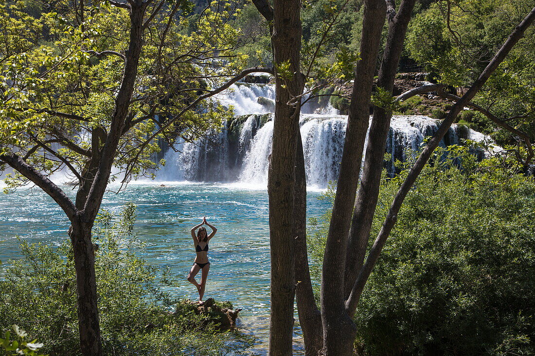 Junge Frau übt Yoga vor Wasserfällen im Krka Nationalpark, nahe Skradin, Šibenik-Knin, Kroatien, Europa
