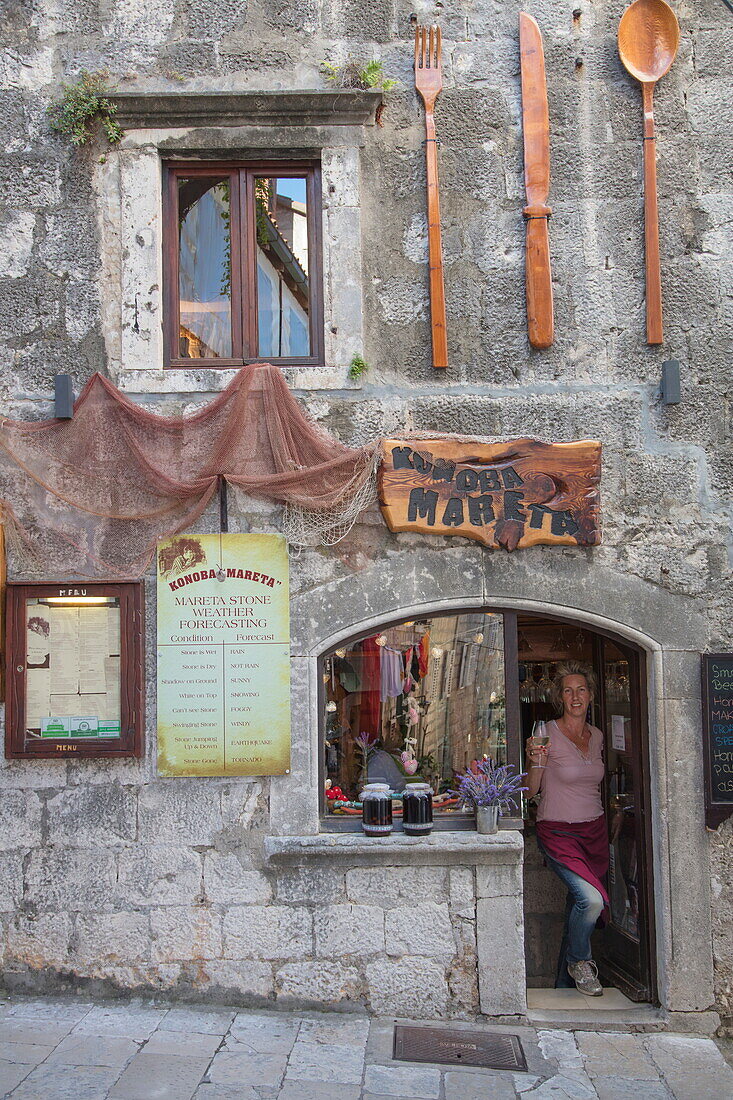 Cheerful waitress with wine glasses in doorway of Konoba Mareta restaurant in Old Town, Korcula, Dubrovnik-Neretva, Croatia