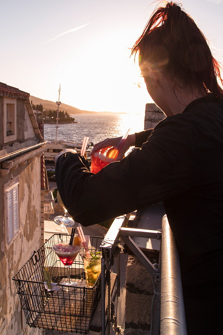 Kellnerin greift nach Tablett mit Getränken die mit Flaschenzug von der Bar auf das Dach der Massimo Cocktail Bar gehoben wurden, die sich im alten Festungsturm in der Altstadt befindet, Korcula, Dubrovnik-Neretva, Kroatien, Europa