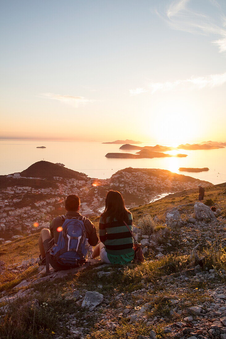Paar genießt Aussicht über die Lapad-Halbinsel und vorgelagerte Inseln, vom Hügel nahe der Bergstatation der Dubrovnik-Gondel bei Sonnenuntergang aus gesehen, Dubrovnik, Dubrovnik-Neretva, Kroatien, Europa