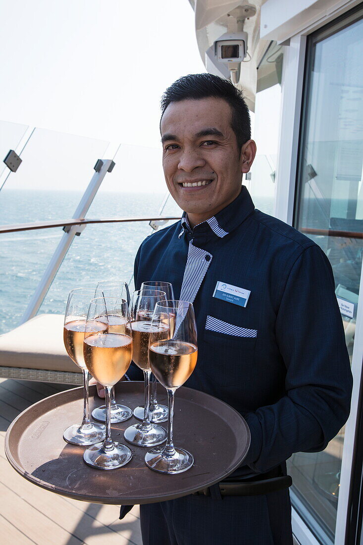 Freundlicher Steward serviert Champagner an Deck vor der X Lounge an Bord von Kreuzfahrtschiff Mein Schiff 6 (TUI Cruises), Ostsee, nahe Dänemark, Europa