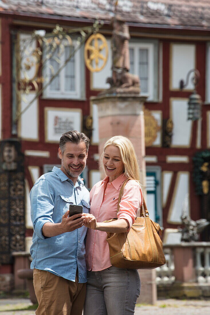 Couple looks at smartphone with half-timbered houses in Altstadt old town behind, Bad Orb, Spessart-Mainland, Hesse, Germany