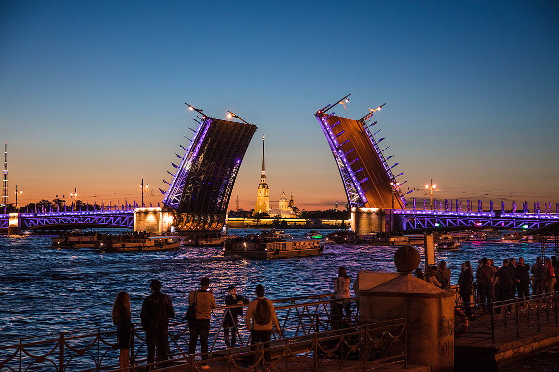 'Crowd admires opening of Dvortsovy bridge (Palace bridge) drawbridge on Neva river with illuminated Peter and Paul Cathedral in Peter and Paul Fortress during ''White Nights'' at dusk, St. Petersburg, Russia'