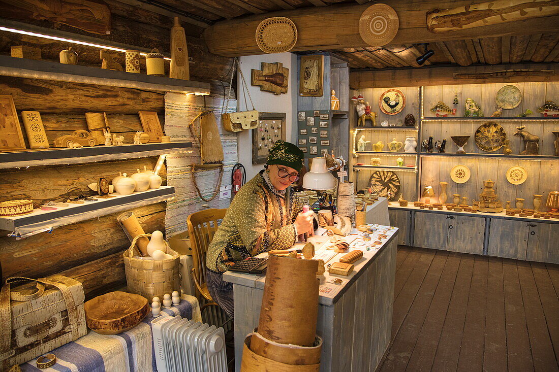 Woman carves wooden artefacts at souvenir stand at Mandrogi crafts village, Mandroga, Svir river, Russia