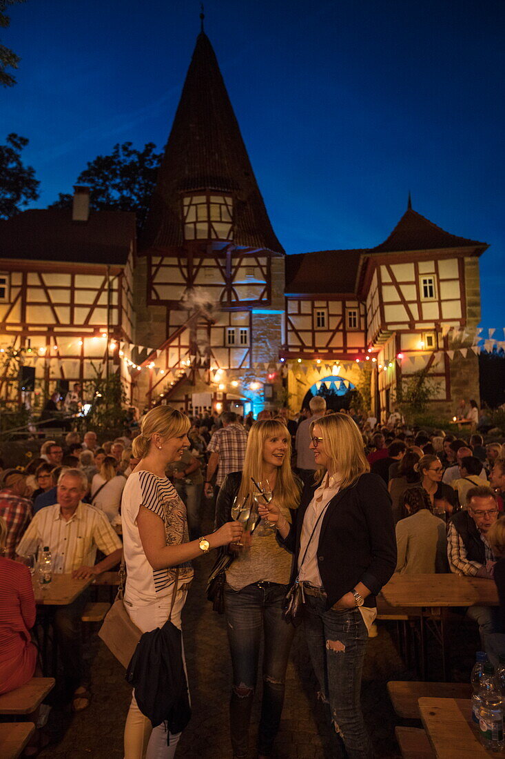 Drei junge Frauen genießen Frankenwein beim Weinfest am Rödelseer Tor in der Abenddämmerung, Iphofen, Fränkisches Weinland, Franken, Bayern, Deutschland, Europa