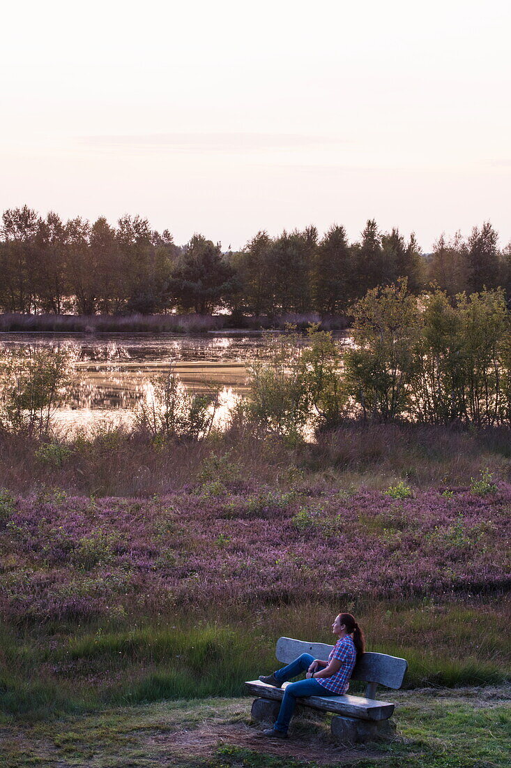Frau blickt auf Moorlandschaft mit Heide und See im Internationalen Naturpark Bourtanger Moor-Bargerveen bei Sonnenuntergang, nahe Twist, Emsland, Niedersachsen, Deutschland, Europa
