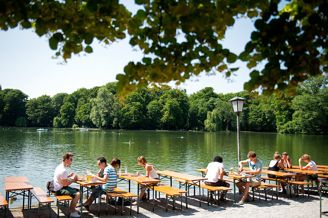 In the beer garden at the Seehaus in the English Garden in Munich, Bavaria, patrons are seated right at the lake