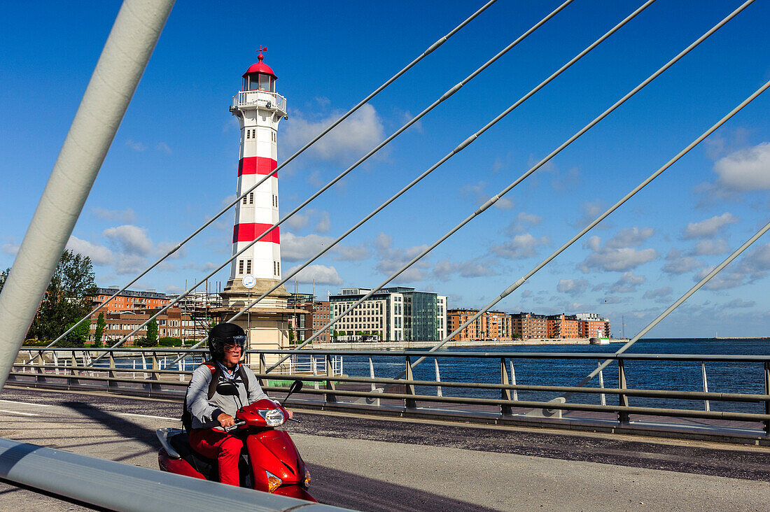 Red white lighthouse in sarnated harbor area, red scooter in foreground on a bridge, Malmo Southern Sweden, Sweden