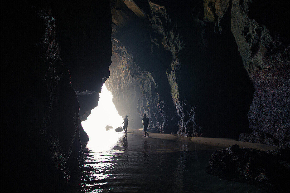 Two young men walking through a cave at the beach Praia da Amoreira,  Aljezur, Faro, Portugal