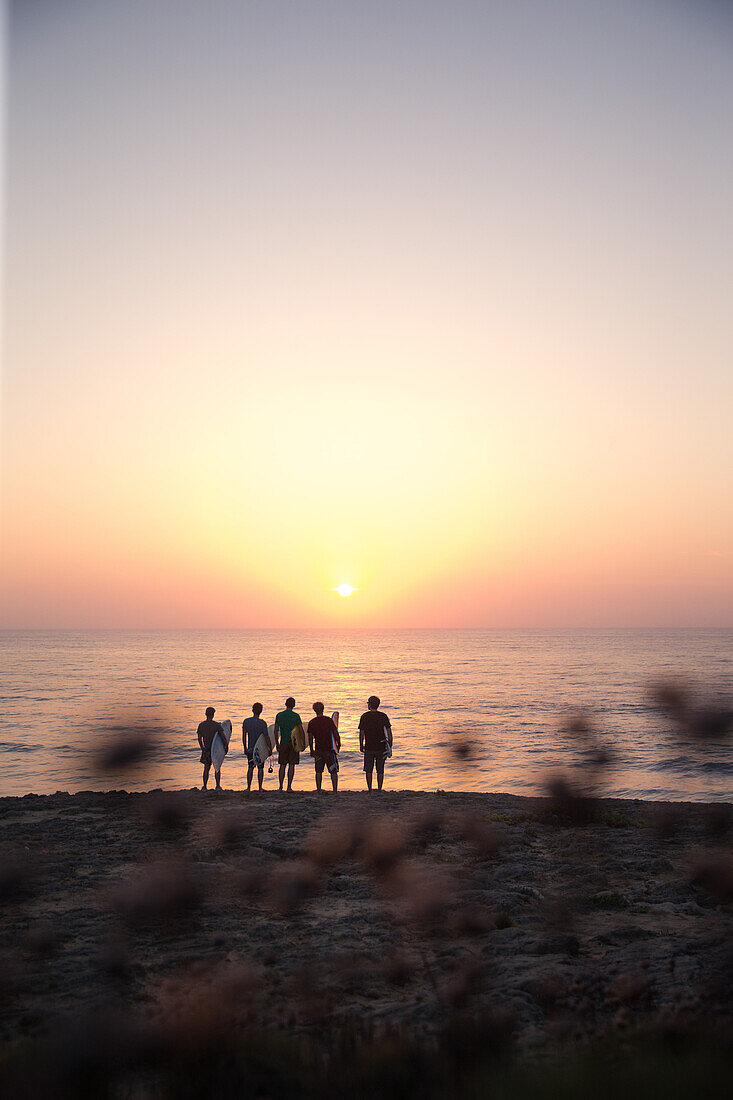 Fünf junge Surfer stehen am Strand von Praia da Amoreira bei Sonnenuntergang,  Aljezur, Faro, Portugal