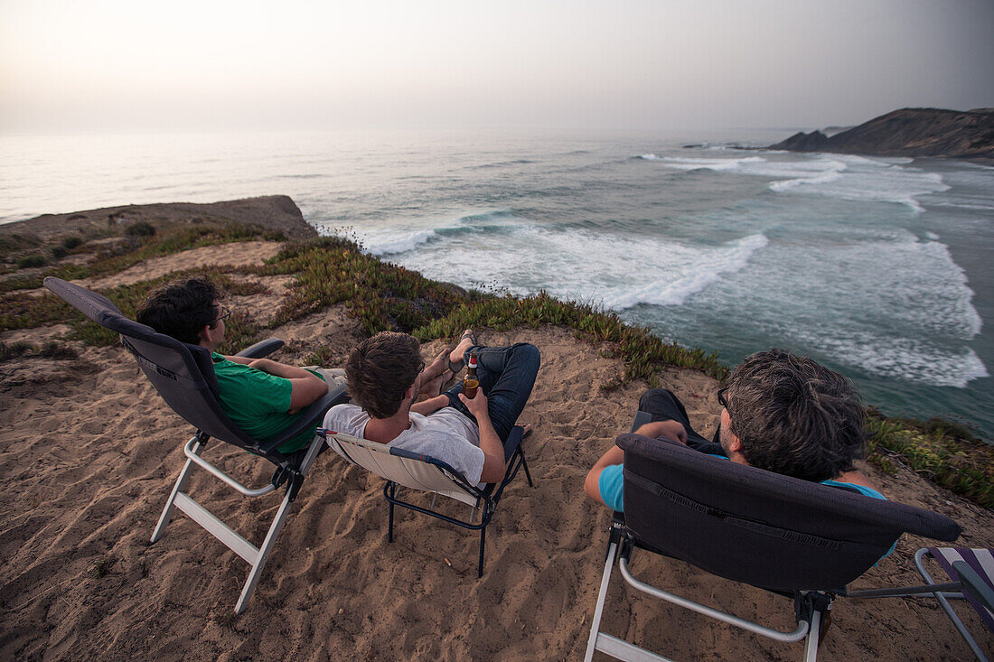 Drei junge Männer genießen den Ausblick auf den Strand Praia da Amoreira,  Aljezur, Faro, Portugal