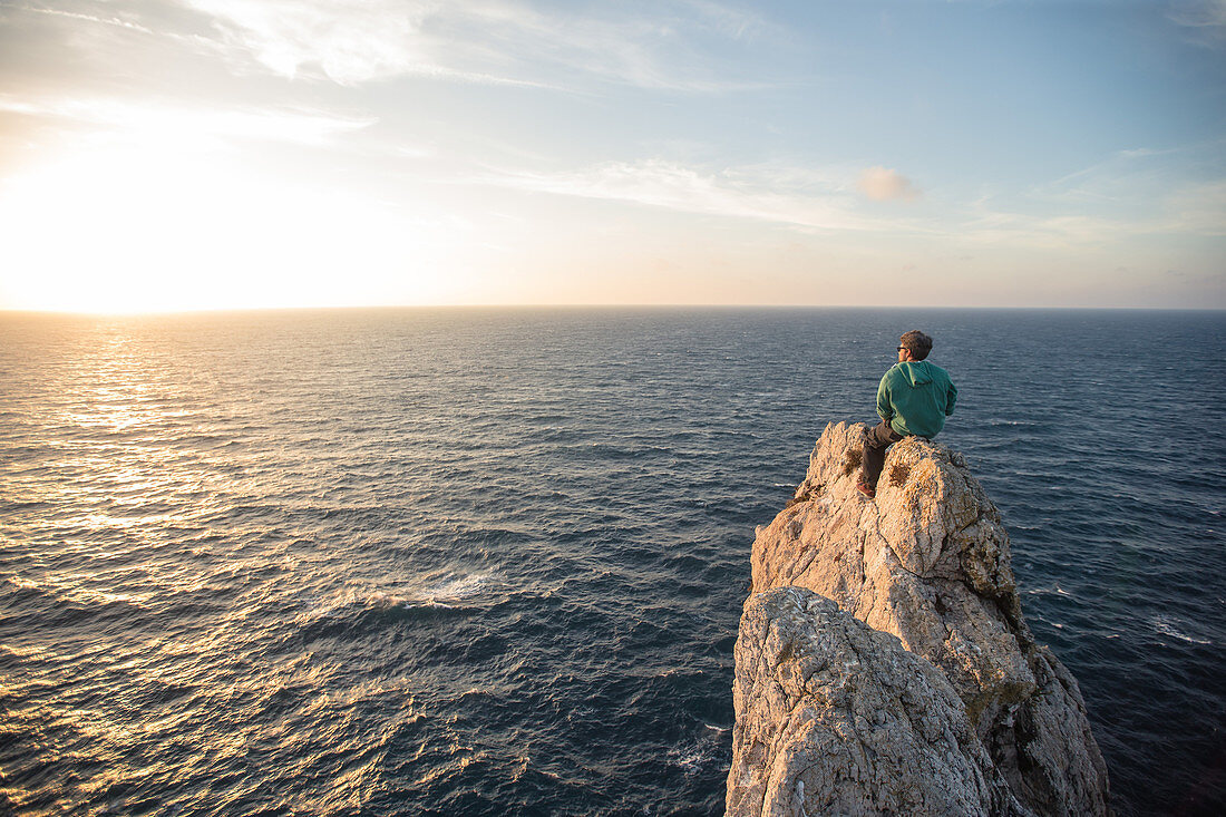 Young man sitting on a cliff edge at the sea at the beach Praia da Amoreira,  Aljezur, Faro, Portugal