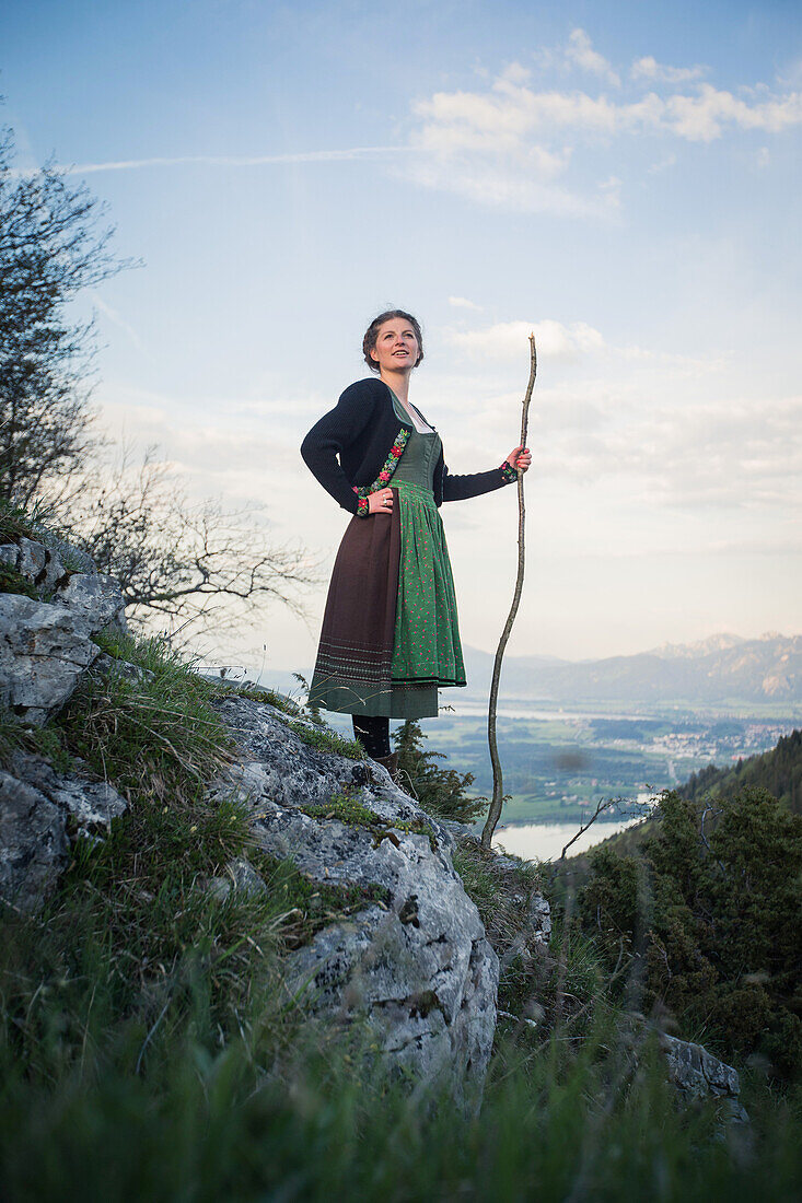 Junge Frau in Tracht steht auf einem Felsen auf dem Falkenstein im Allgäu, Pfronten, Bayern, Deutschland