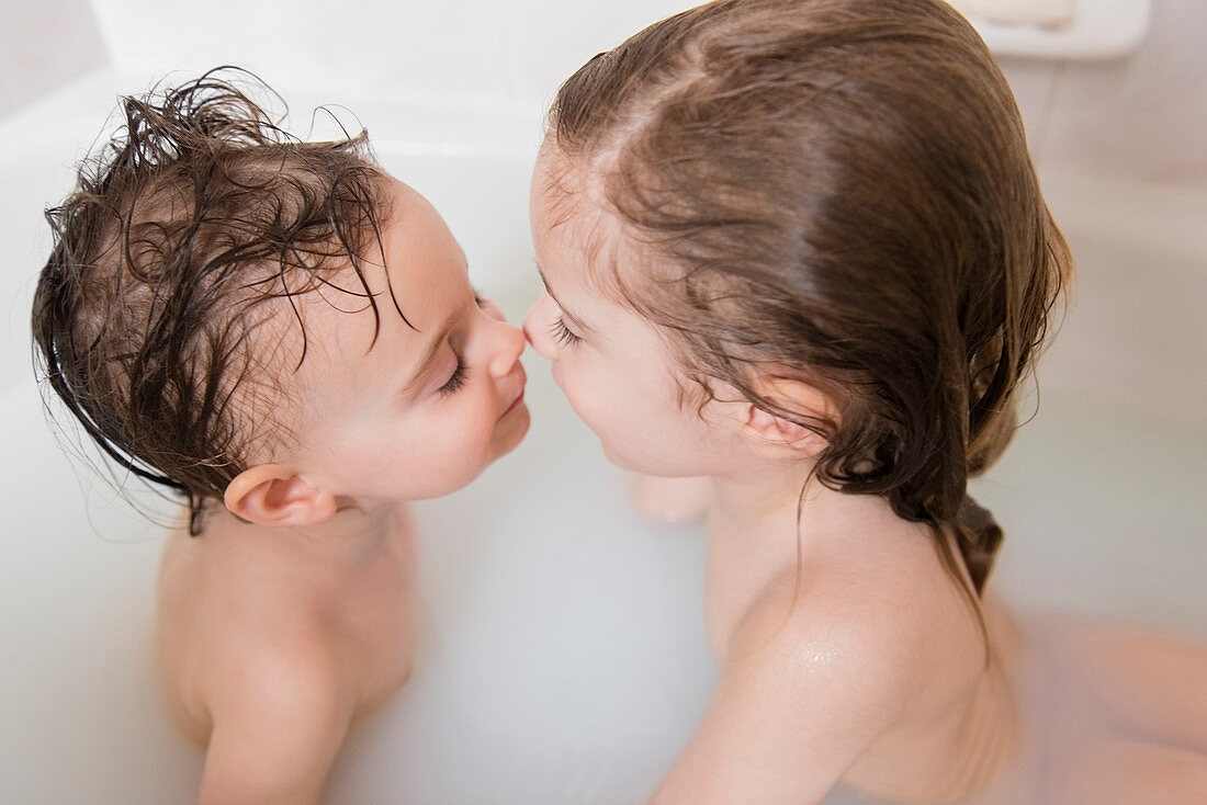 Caucasian boy and girl rubbing noses in bathtub