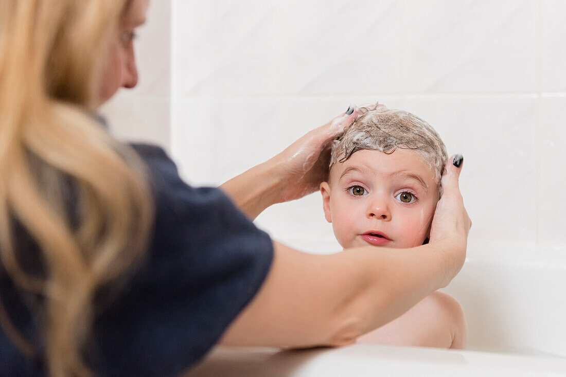 Caucasian mother washing hair of girl in bathtub