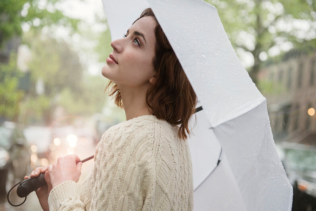 Caucasian woman holding umbrella looking up