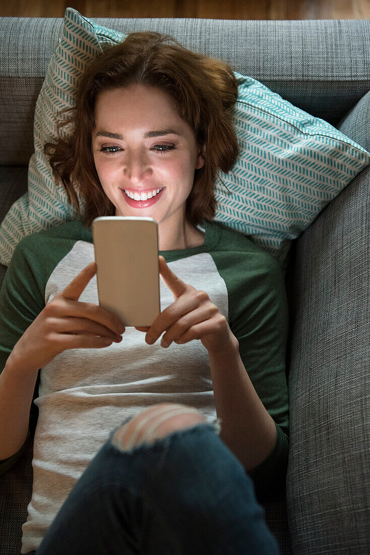 Caucasian woman laying on sofa texting on cell phone