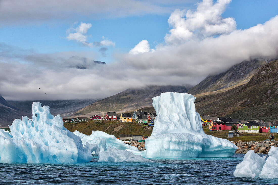 icebergs that separated from the glacier snouts in the fjord in front of the colorful wooden houses of the village of narsaq, greenland