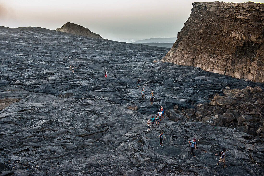 Tourists walking through lava field around the very active Erta Ale shield volcano, Danakil depression, Ethiopia, Africa