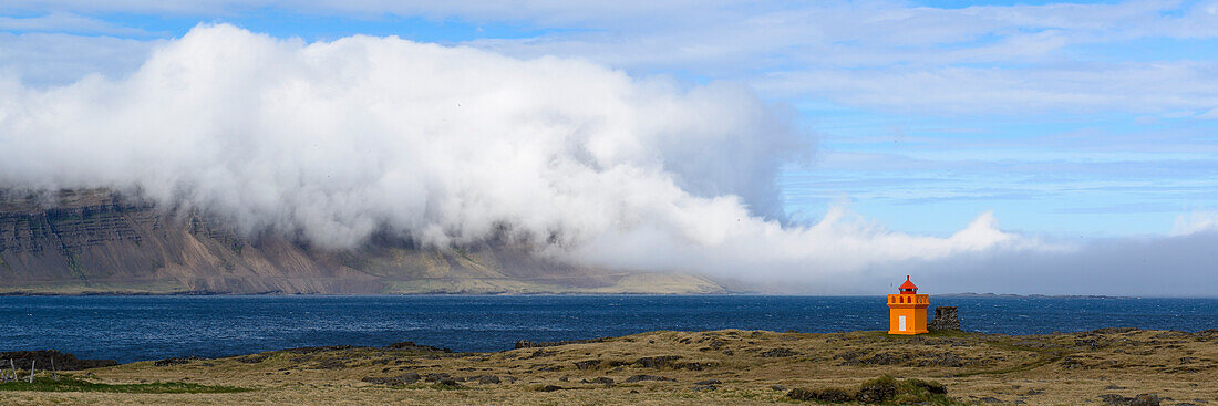 tiny orange lighthouse and sea fog at the eastfjords of Iceland