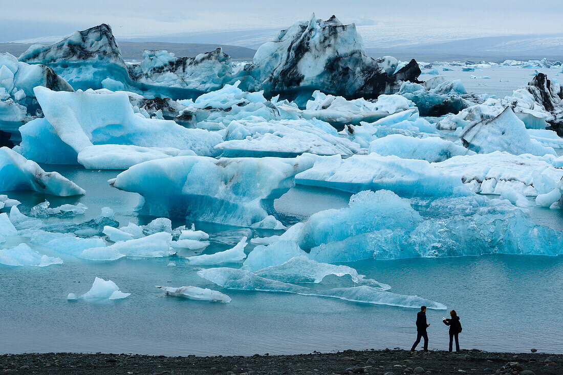 Zwei Touristen bestaunen die Eisberge in der Gletscher Lagune Jokulsarlon im Süden Islands