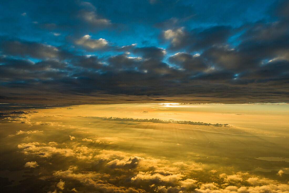 Die dünne Wolkendecke trennt den blauen Himmel vom warmen Licht der tief stehenden Sonne, Luftaufnahme