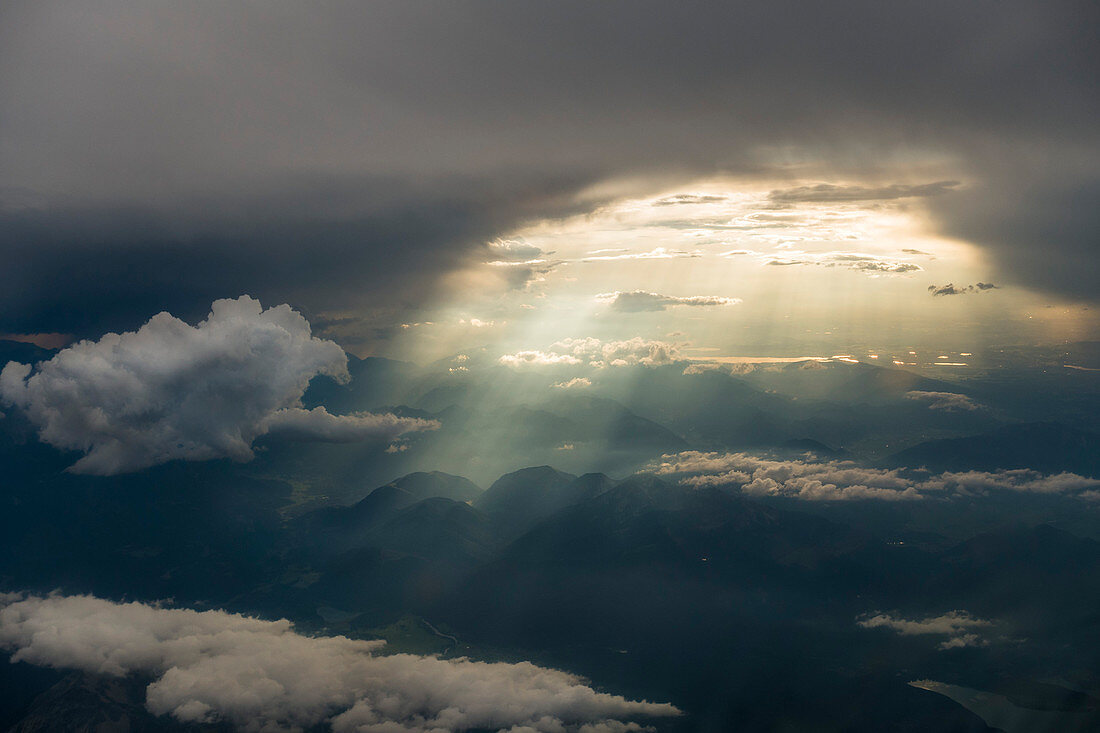 Sonnenstrahlen brechen durch ein Wolkenloch und beleuchten die Hügel der norditalienischen Alpen, Luftaufnahme, nordwestlich von Mailand, Italien
