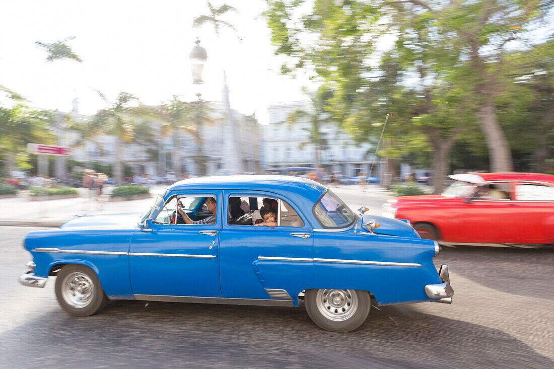 blue and red oldtimer driving along Central Park, parque central, historic town, center, old town, Habana Vieja, Habana Centro, family travel to Cuba, holiday, time-out, adventure, Havana, Cuba, Caribbean island