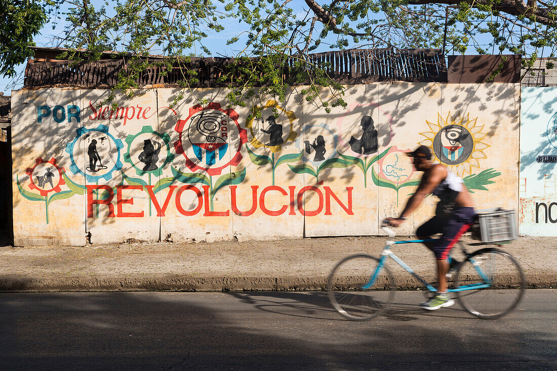 Fahrradfahrer, Fahrrad, auf einer der wenig befahrenen Straßen, Hausfassade mit Revolution Graffiti, por Siempre Revolucion, gut erhaltene koloniale Altstadt, historische Bausubstanz, Perle des Südens,  Familienreise nach Kuba, Auszeit, Elternzeit, Urlaub
