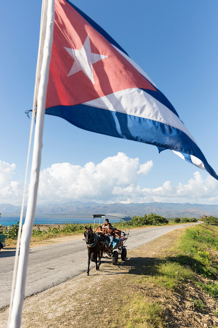 the cuban flag flying at the snorkeling snack bar La Batea, horse-drawn carriage on a lonely coast road from La Boca to Playa Ancon, with beautiful small beaches in between, at the beach, turquoise blue sea, family travel to Cuba, parental leave, holiday,
