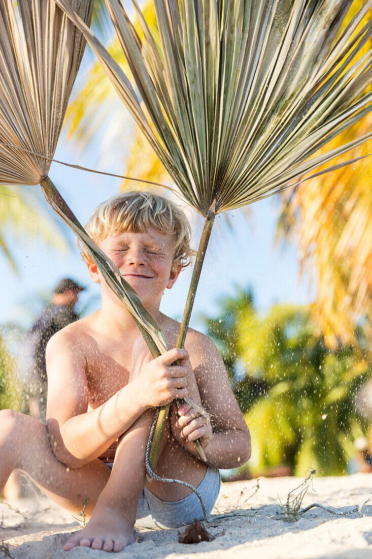 Junge, 6 Jahre, spielt mit Palmenblättern am schönen Sandstrand von Playa Ancon, Sand, türkisblaues Meer, schnorcheln, Familienreise nach Kuba, Auszeit, Elternzeit, Urlaub, Abenteuer, MR; bei La Boca und Trinidad, Republik Kuba, karibische Insel, Karibik