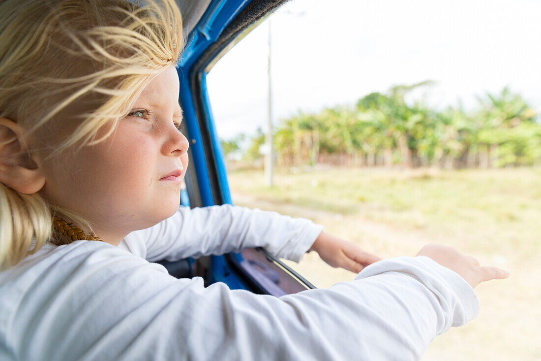 girl looking out of the window, hair blowing in the wind, on the way from Cayo Coco to Santa Clara, on the road, empty street, no traffic, horse-drawn carriage, horse, transport, oldtimer, blue, family travel to Cuba, parental leave, holiday, time-out, ad