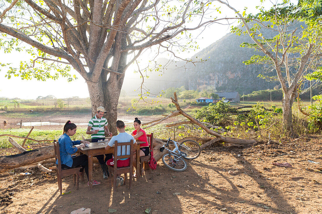 Friends playing cards at a table next to fields, Mogotes and tobacco fields in Vinales, climbing region, loneliness, beautiful nature, family travel to Cuba, parental leave, holiday, time-out, adventure, National Park Vinales, Vinales, Pinar del Rio, Cuba