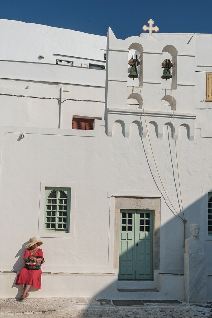 Woman in red dress and straw hat on white stone ledge outside the church, Kastro Village, Sifnos, Cyclades, Greek Islands, Greece, Europe